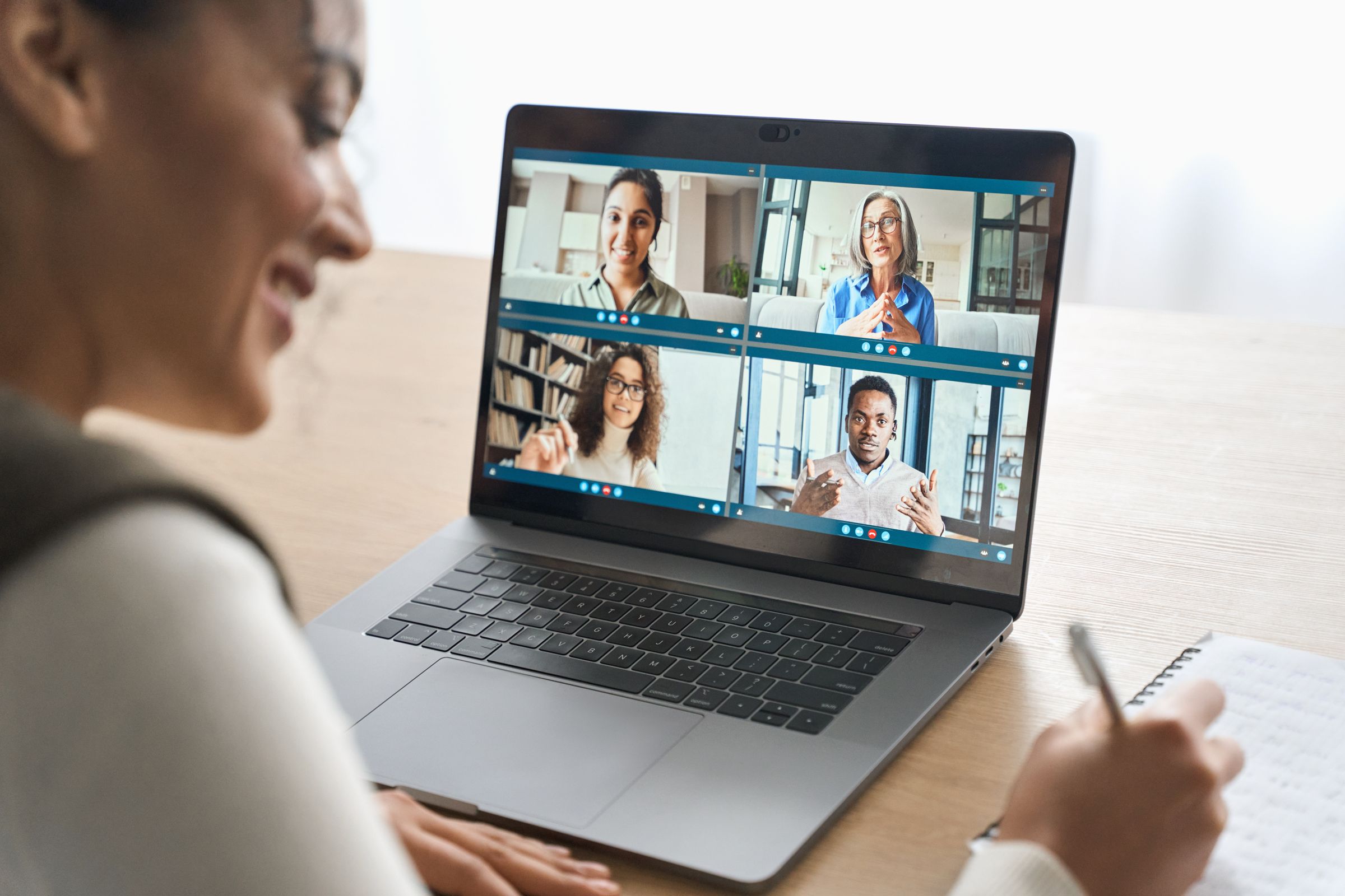 A woman smiling at a video call on her laptop, with four people on screen.